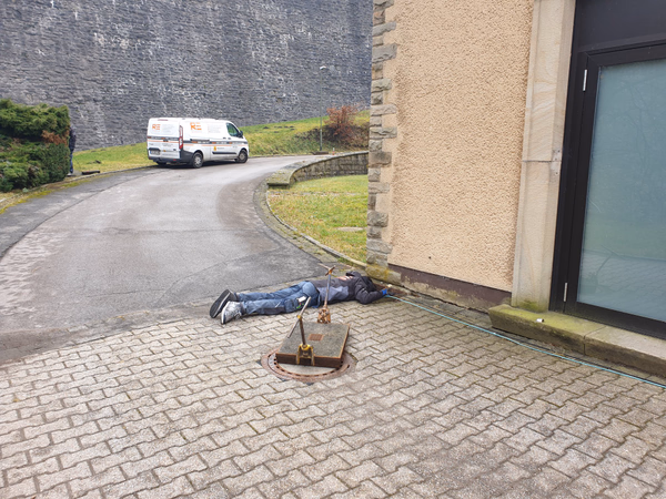 Elektriker liegt vor einem geöffneten Kabelschacht und verlegt ein Glasfaserkabel an einem Gebäude